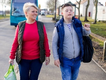 A person with disability walking with a family member on a street. They are smiling.