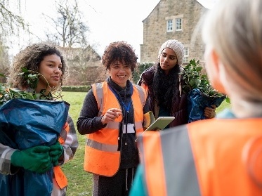 A person wearing a work vest and instructing a group of people working outside.