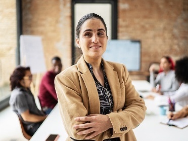 A person standing in front of a conference table with a group of people sitting behind them.