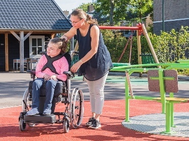 A child with a disability and their carer using a playground.